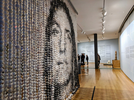 An artwork with hanging beads and an Indigenous woman's face printed on them titled "Every One" by Cannupa Hanska Luger.