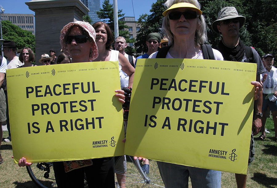 Two women hold signs that say "Peaceful protest is a right" at a rally in support of civil liberties.